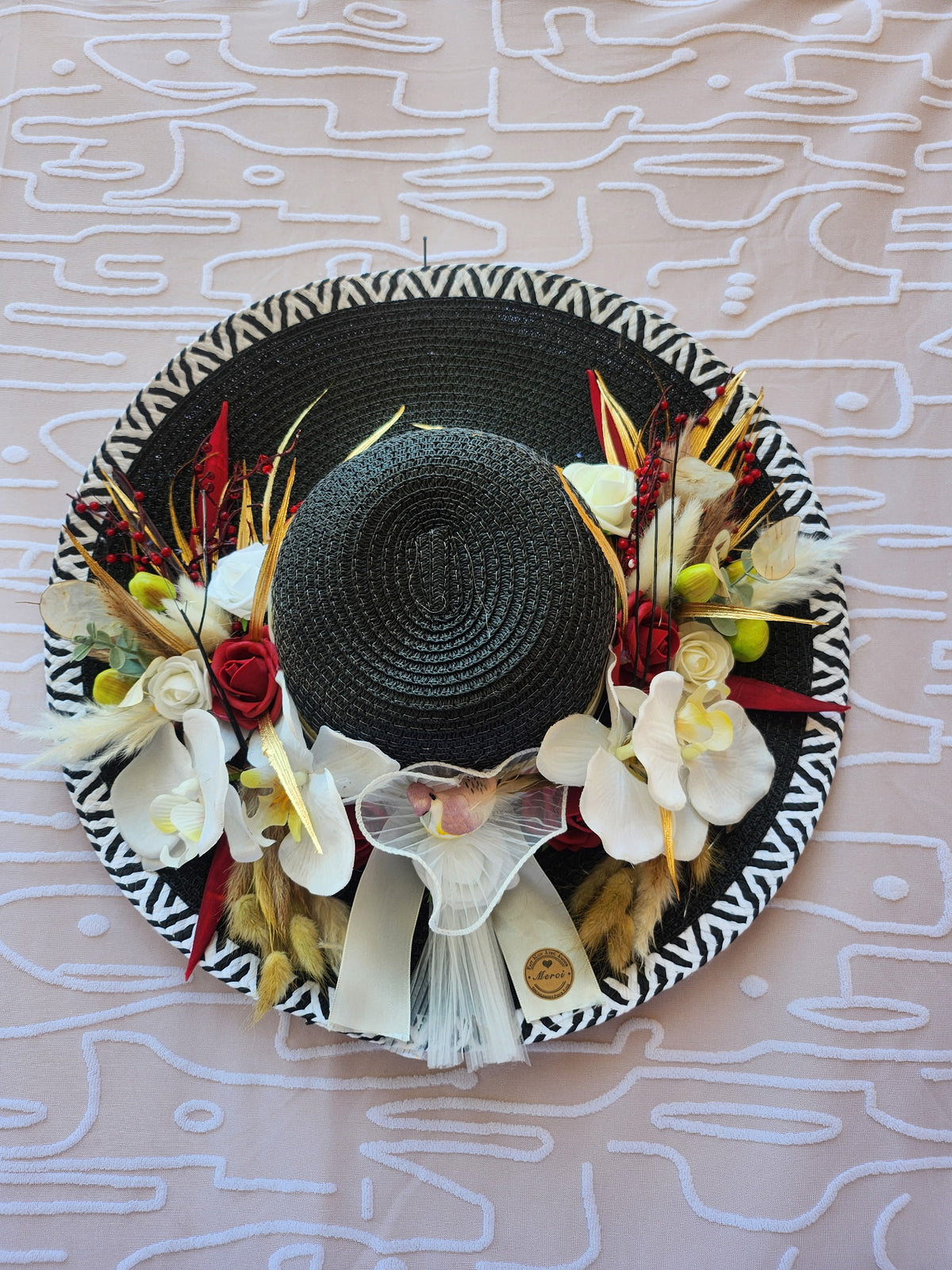 Chapeau de paille noir zébré orné d'orchidées blanches, roses rouges et fleurs séchées